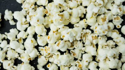 A close-up view of freshly popped popcorn scattered on a dark surface, ideal as a snack.