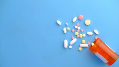 An assortment of colorful pills scattered from a prescription bottle on a blue background.