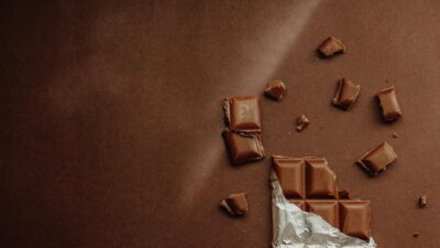 A tempting dark chocolate bar partially unwrapped on a textured brown surface, highlighting its richness.
