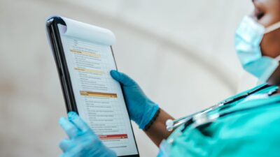 Side view of crop African American female medic in uniform reading text on paper at work