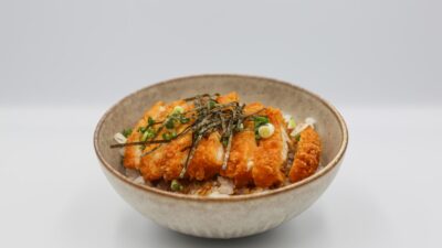 a bowl filled with rice and meat covered in sauce