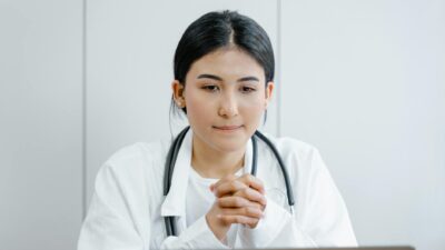Young female doctor in white coat consulting online with stethoscope indoors.