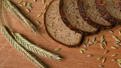 A rustic arrangement of sliced wheat bread with wheat ears and grains on a wooden surface.