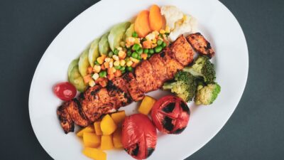 grilled meat with sliced lemon and sliced tomatoes on white ceramic plate