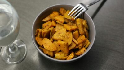 From above sliced fried sweet potato served in ceramic bowl with fork and glass of water on table