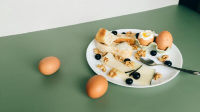Plate of cheese, boiled eggs, bread, walnuts, and blueberries for a hearty breakfast.