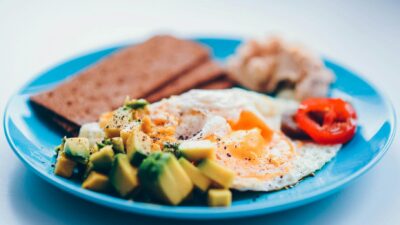 Bright and colorful breakfast featuring fried eggs, avocado, and fresh vegetables on a blue plate.