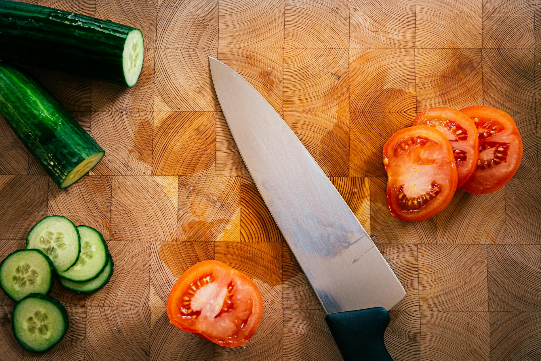 Close-up of fresh cucumbers and tomatoes being sliced on a wooden chopping board.