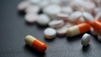 Assorted pills and capsules on a dark background, emphasizing medication variety.