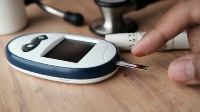 Close-up image of a glucometer checking blood sugar level with a finger pricking device nearby.