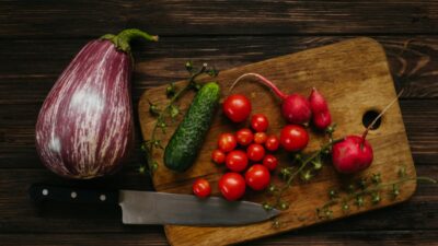 A variety of fresh vegetables with a knife on a rustic wooden cutting board.