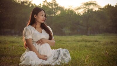 A pregnant woman sitting in a field at sunset