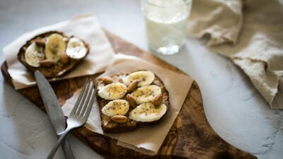 Delicious sliced banana and almond toast on rustic wooden board with milk glass, perfect for breakfast.