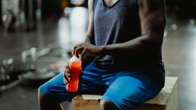 Muscular man taking a break with a sports drink in a gym setting.