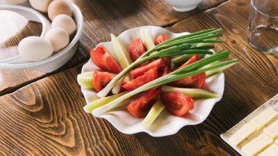 A vibrant plate of fresh tomatoes, cucumbers, and chives next to eggs on a wooden table.