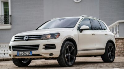 A white Volkswagen Touareg SUV parked on a city pavement with a modern building backdrop.