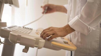 Healthcare worker operating advanced ultrasound machine in medical setting.
