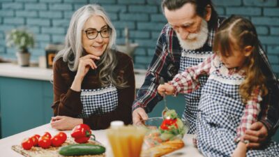 Grandparents and a child enjoy cooking together in a warm kitchen setting.