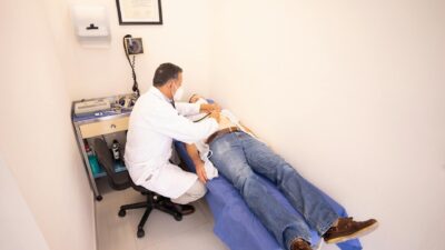 Medical professional examines patient with stethoscope in clinic examination room.