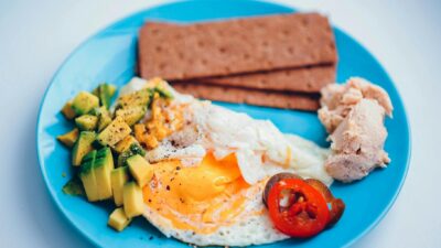 A vibrant breakfast plate with fried egg, avocado, crispbread, and chicken.