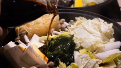 Sauce being poured into a hot pot with vegetables.