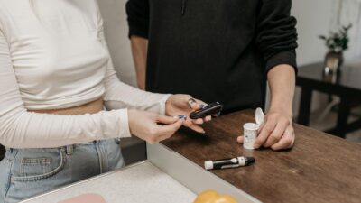 Two adults checking blood sugar with a glucometer and insulin pen on a wooden table.