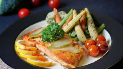 Colorful plate of grilled fish garnished with lemon, pickles, and fresh vegetables. Perfect for healthy meal inspiration.