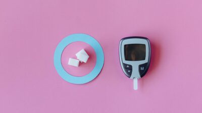 Flat lay of glucometer with sugar cubes on pink background, symbolizing diabetes awareness.