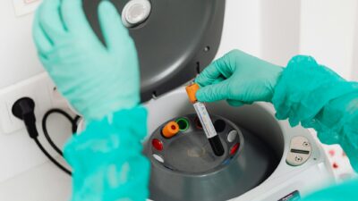 A lab technician wearing gloves uses a centrifuge for blood analysis in a modern laboratory setting.