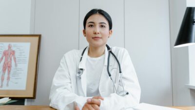 Young female doctor sitting at desk with stethoscope, ready for telehealth consultation.
