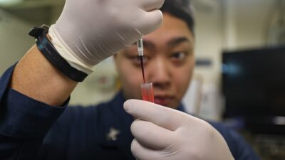 A person in gloves carefully transfers liquid into a vial.