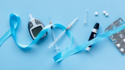 Flat lay of diabetes management tools with blue ribbon symbolizing awareness on a light blue background.