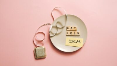 Flat lay of a plate with scrabble tiles spelling 'Eat Less Sugar,' accompanied by a tape measure, symbolizing healthy eating.