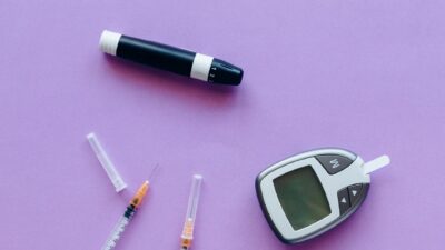 Top view of diabetes management tools including glucose meter and insulin syringes on purple background.