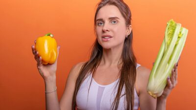 Woman holding yellow bell pepper and celery, showcasing healthy eating.