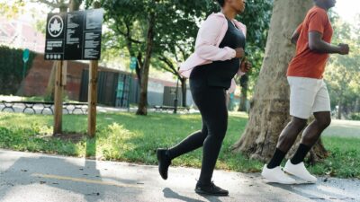 Two adults jogging on a sunny day in a green park, promoting fitness.
