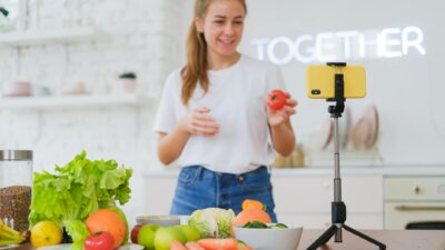 Young woman filming a healthy cooking video in a bright modern kitchen with fresh vegetables.