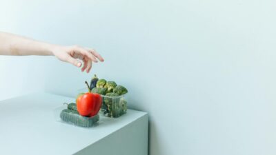Hand reaching for fresh vegetables on a minimalist white surface.