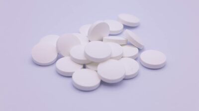 Assorted white tablets stacked on a soft purple surface, symbolizing medication and healthcare.