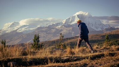 A person hiking through a mountainous region with snow-covered peaks at sunset, offering a serene outdoor experience.