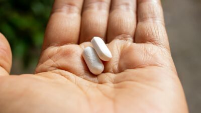 An intimate close-up of two pills held in a person's open palm against a blurred outdoor background.