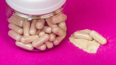 A glass jar filled with capsules alongside loose powder on a vibrant pink background.