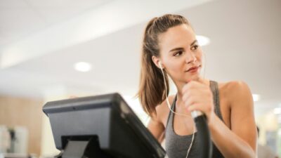 Fit woman working out on an elliptical machine indoors, wearing headphones and a sports bra.