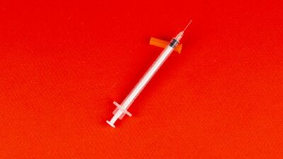 A syringe lying on a vivid red background, captured from above, signifying medical themes.