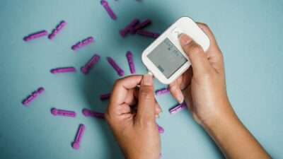 Top view of crop anonymous female diabetic measuring blood sugar with glucometer over scattered lancets