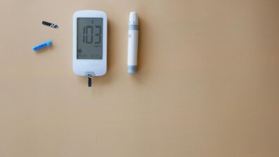 Blood glucose meter, test strip, and lancet on beige background for diabetes monitoring.