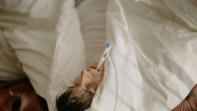 A man lying in bed with a thermometer in his mouth, wrapped in cozy bedding, indicating illness or fever.