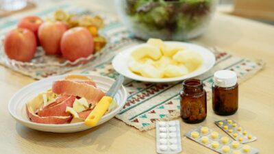 From above of various medicines placed on table near plates with fresh peeled apples and bowl of salad in kitchen