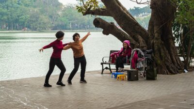 Two women dance by a lake, another sits nearby.