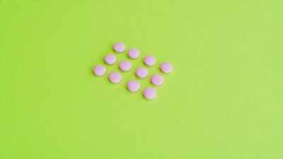 Minimalist photo of pink pills arranged on a vibrant green background.
